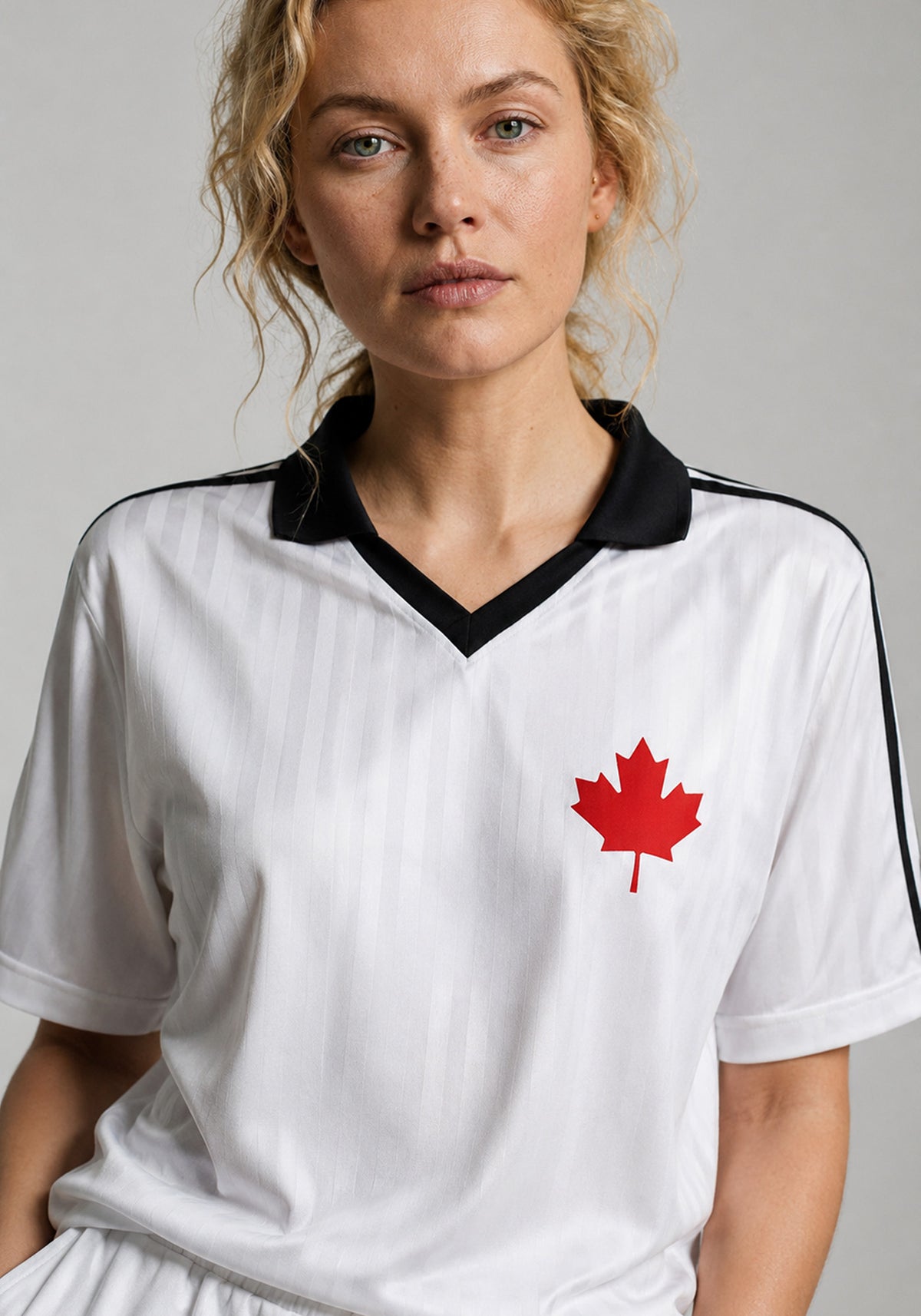 A close-up studio portrait of a woman with curly blonde hair wearing the white heritage soccer jersey. The shot highlights the crisp black collar detail and the fabric’s textured vertical stripes.