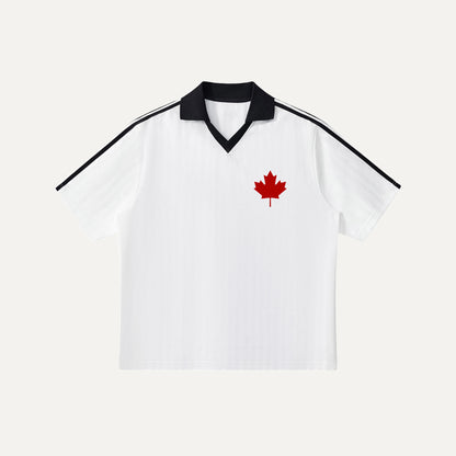 A flat-lay view of a white soccer jersey featuring a subtle vertical jacquard pattern, a sharp black contrast V-neck collar, and a vibrant red maple leaf logo on the left chest.