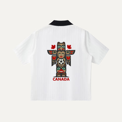 The back of a white soccer jersey showcasing a large, colorful Indigenous-inspired totem pole graphic in the center, with the word "CANADA" and two small red maple leaves printed in red below it.
