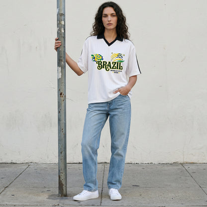 Woman wearing a Brazil World Cup t-shirt and jeans standing against a plain wall.