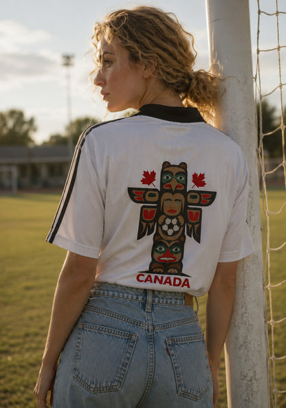 A sunset lifestyle photograph of a model leaning against a soccer net, highlighting the bold totem graphic on the back of the jersey against the soft-focus background of an athletic field.