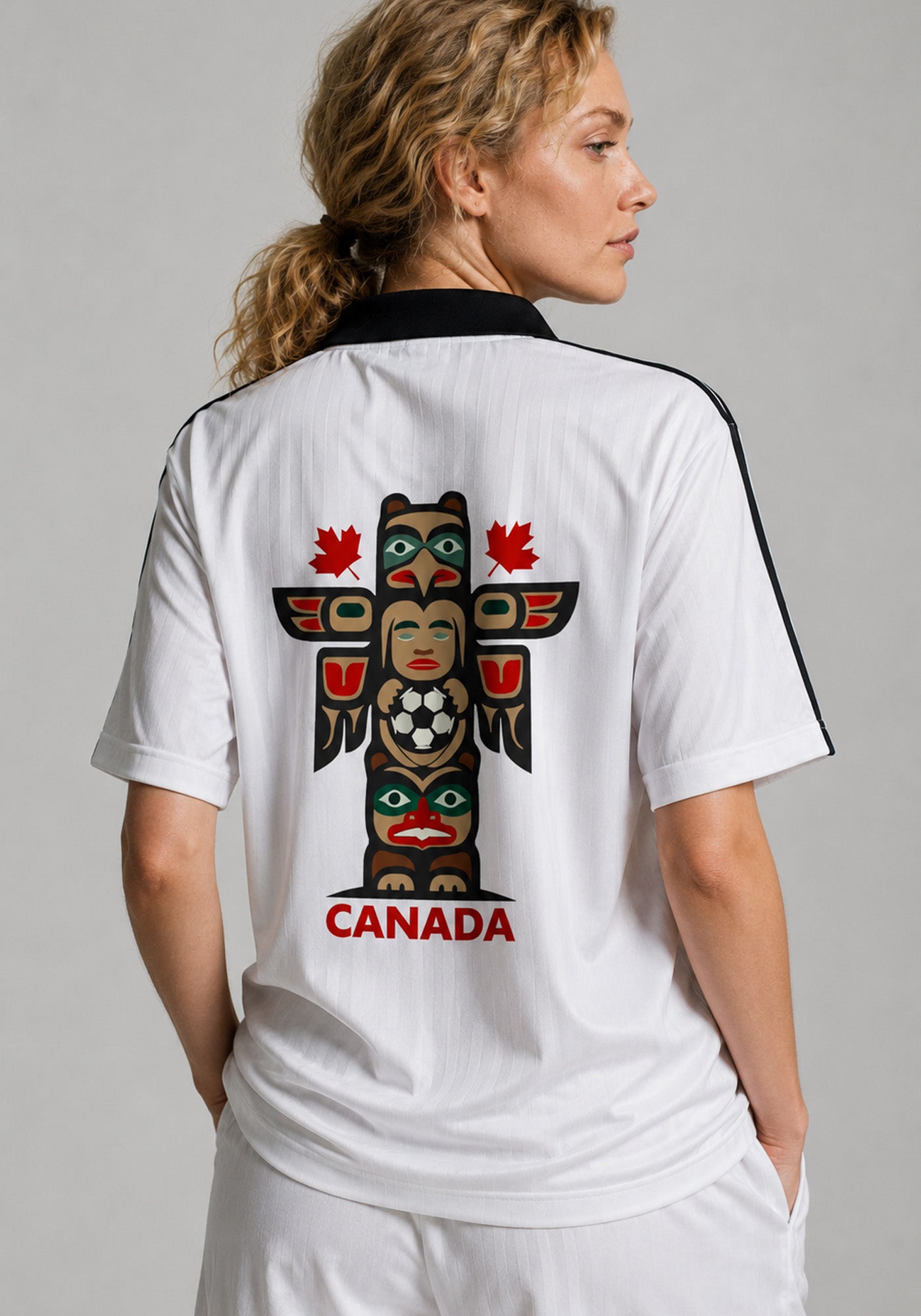 A studio shot of a model from the back, looking over her shoulder to prominently display the large Emily Carr-inspired totem pole artwork and "CANADA" text across the center of the jersey.