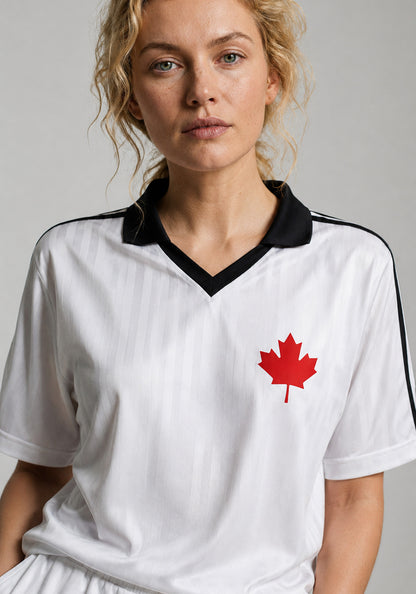 A close-up studio portrait of a woman with curly blonde hair wearing the white heritage soccer jersey. The shot highlights the crisp black collar detail and the fabric’s textured vertical stripes.