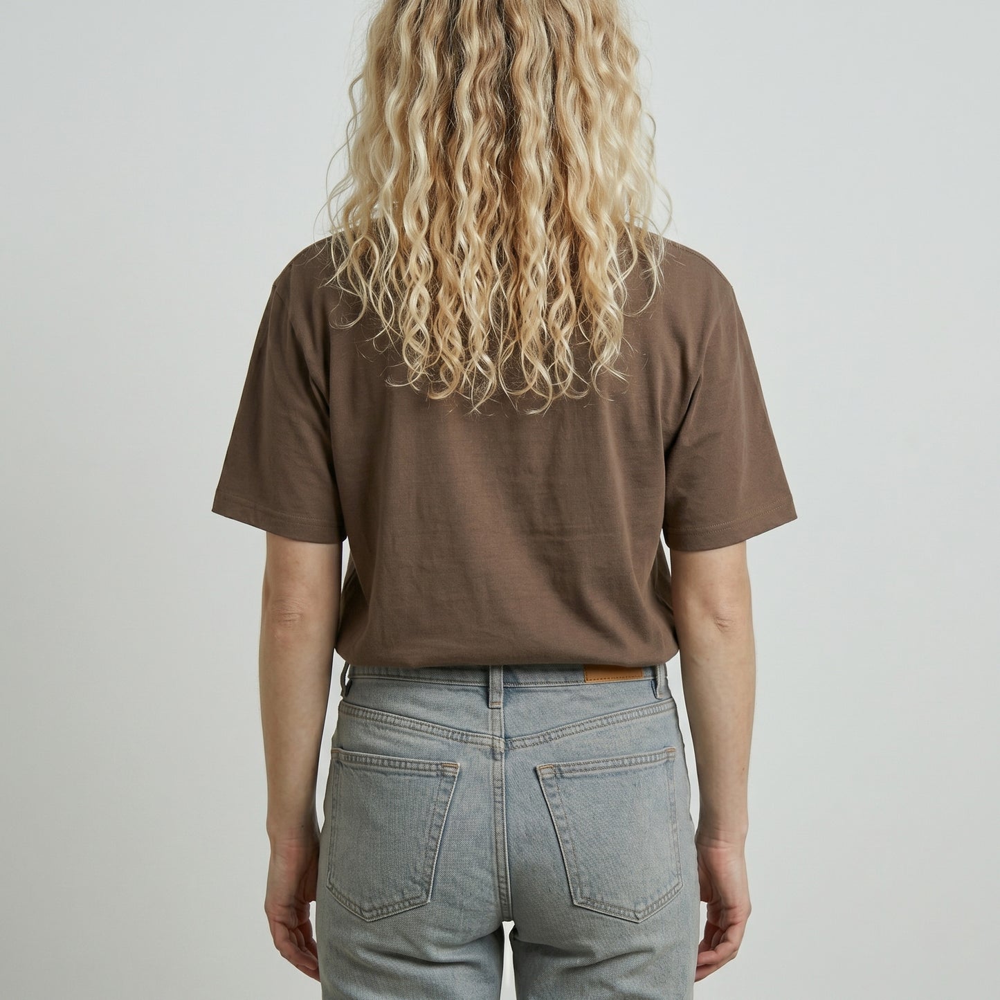 Person wearing a brown t-shirt and light blue jeans against a plain background