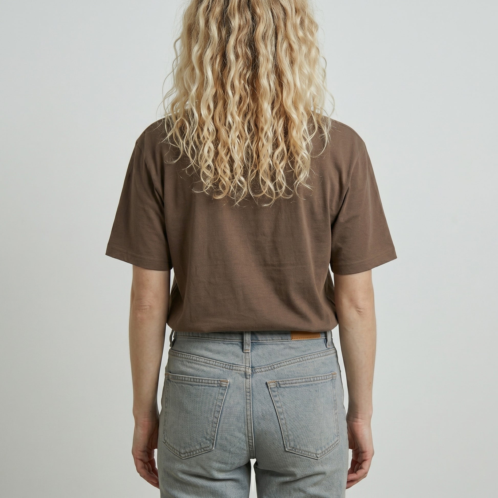 Person wearing a brown t-shirt and light blue jeans against a plain background