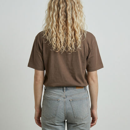 Person wearing a brown t-shirt and light blue jeans against a plain background