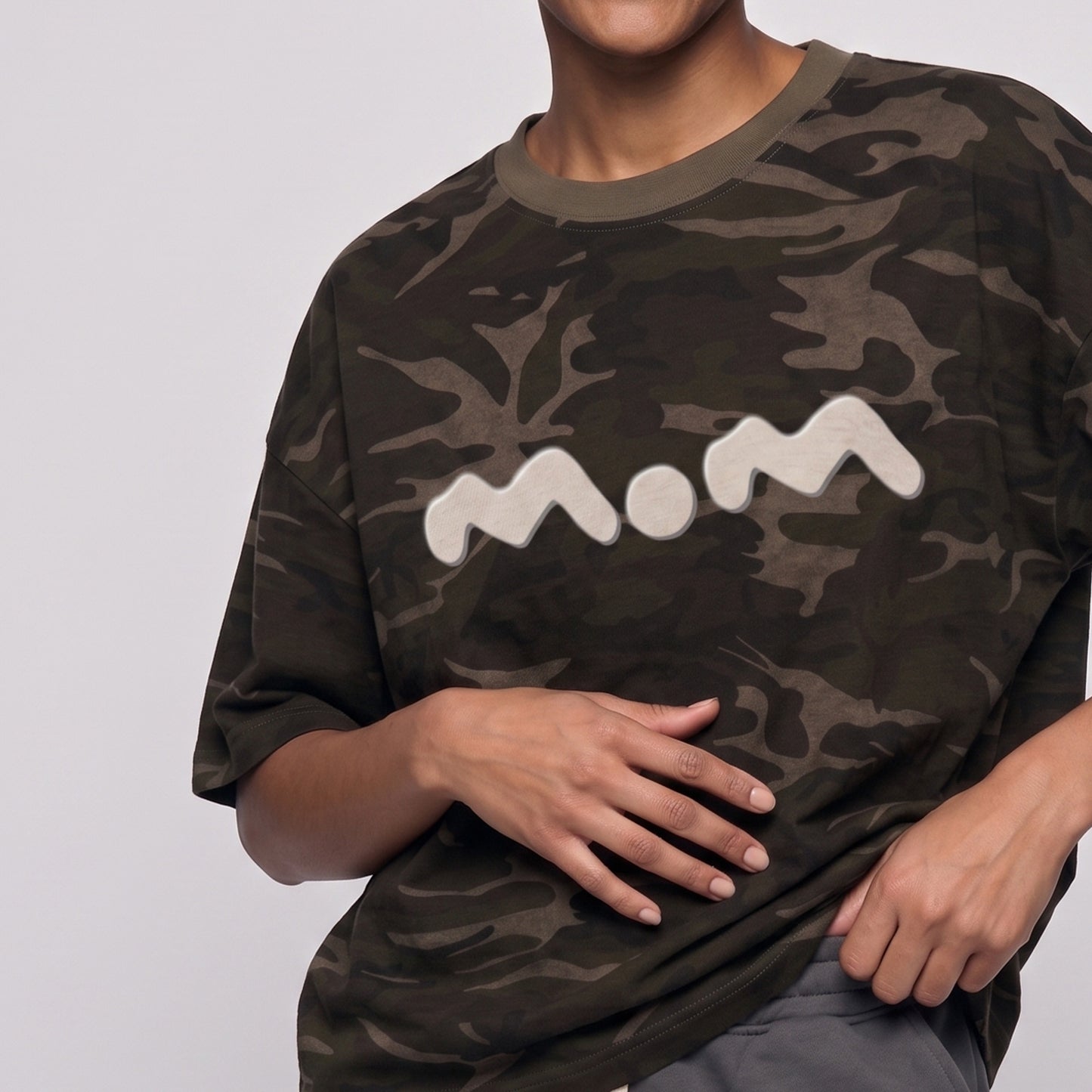 Person wearing a camouflage t-shirt with 'mom' printed on it against a plain background