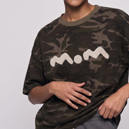 Person wearing a camouflage t-shirt with 'mom' printed on it against a plain background
