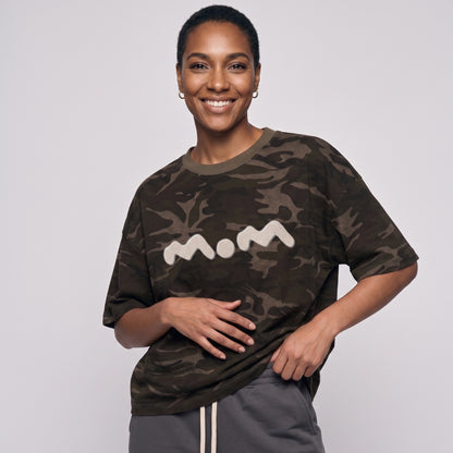 Person wearing a camouflage t-shirt with 'mom' printed on it against a plain background