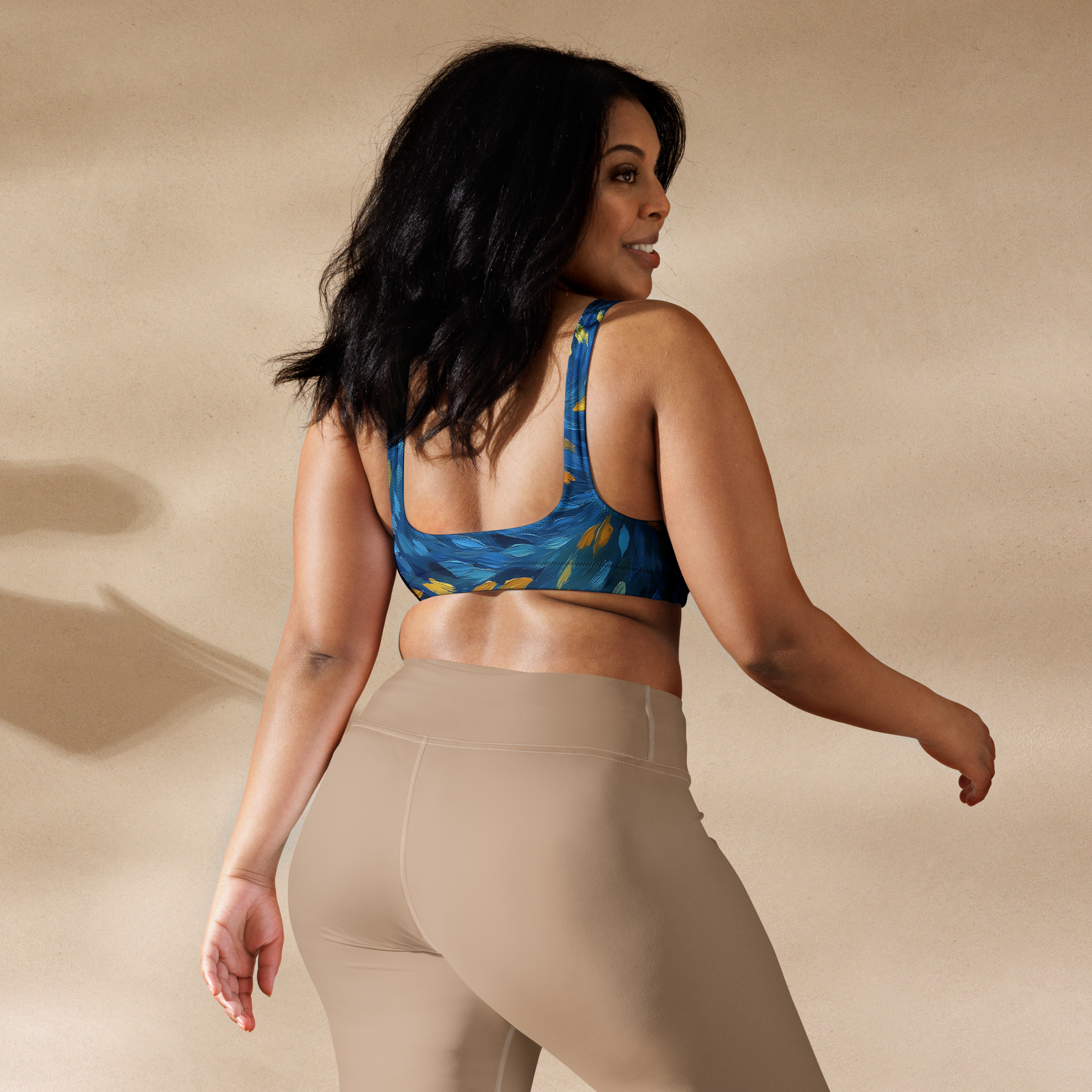 Woman wearing a blue patterned sports bra and beige leggings on a beige background