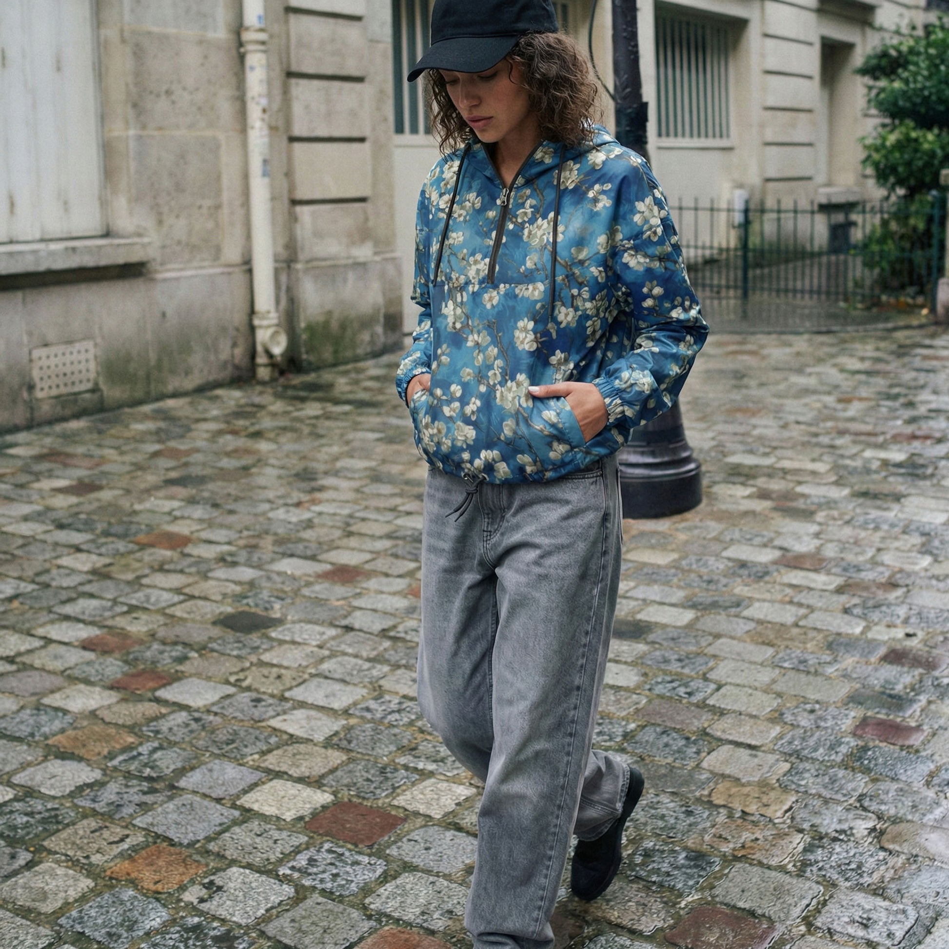 Person wearing a blue floral jacket and gray pants walking on a cobblestone street.