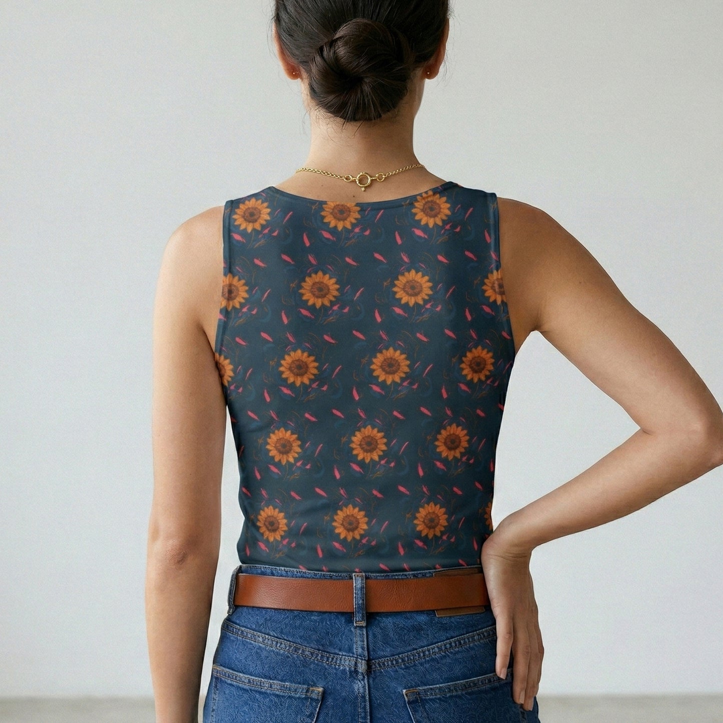 Person wearing a sleeveless top with sunflower pattern and blue jeans against a plain background