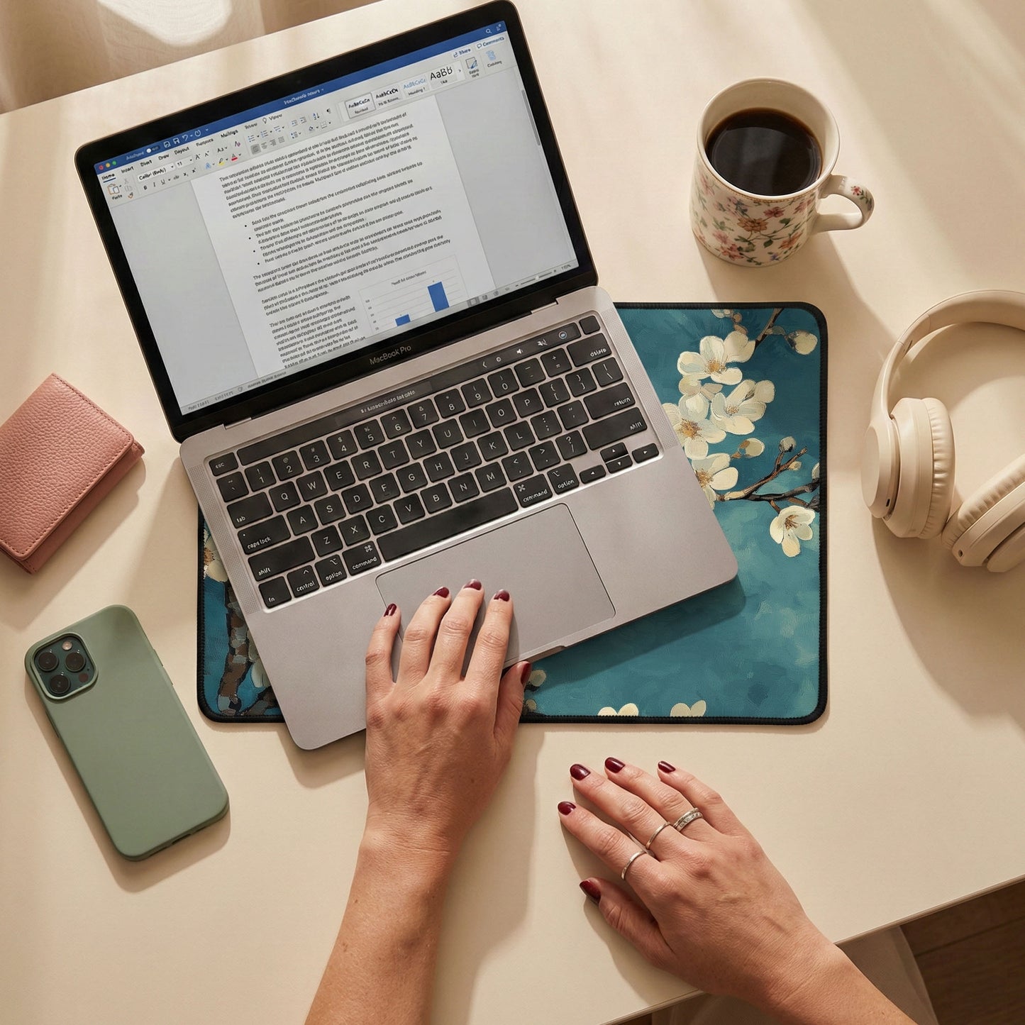 Person using a laptop on a desk with a phone, coffee cup, and headphones nearby.